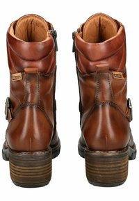 Botas de tobillo de cuero marrón con un lado con cremallera, diseño texturizado, tacón de madera acanalado y un acento de hebilla ajustable en el lado.