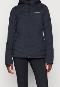 Giacca a vento in navy scuro, con cappuccio, design a motivo diagonale, zip frontale e dettaglio del logo sul petto.