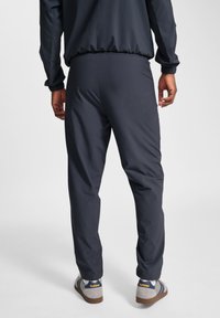 Donkergrijze sportbroek met een tapering fit, gemaakt van glad, lichtgewicht materiaal; gecombineerd met casual schoeisel met blauwe en grijze accenten.