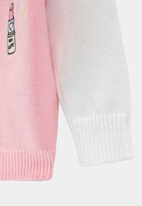 Pull en tricot rose et blanc avec un ourlet côtelé. Présente un détail brodé de rouge à lèvres. Texture douce, design décontracté.
