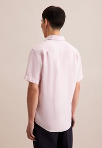 Korte mouwen shirt van lichtroze stof met een gestructureerde afwerking, met een klassieke kraag en een afgeronde zoom, gedragen door een persoon van achteren.