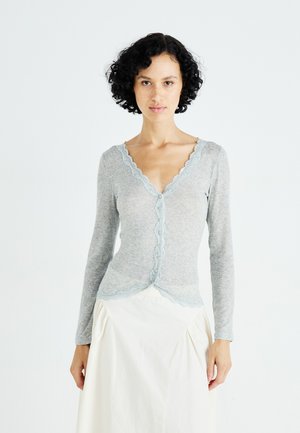 Light gray long-sleeve cardigan with scalloped lace trim and button closure. Soft fabric with textured ribbing, paired with a white skirt.