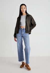 Dark green leather bomber jacket with elastic cuffs, gray cropped top, light blue wide-leg jeans, and brown athletic sneakers.