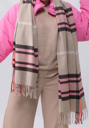 Écharpe beige à motif à carreaux rose, noir et blanc avec des extrémités frangées, portée avec un pantalon beige et une veste matelassée rose.