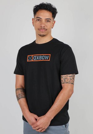 T-shirt en coton noir à manches courtes et col rond. Présente un logo rectangulaire "OXBOW" en orange et bleu sur le devant.