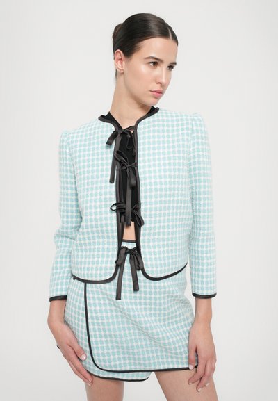 Lyseblå rutete jakke med svart kant og sløyfer, kombinert med et matchende skjørt. Glatt tekstur, fitted design og cropped stil.