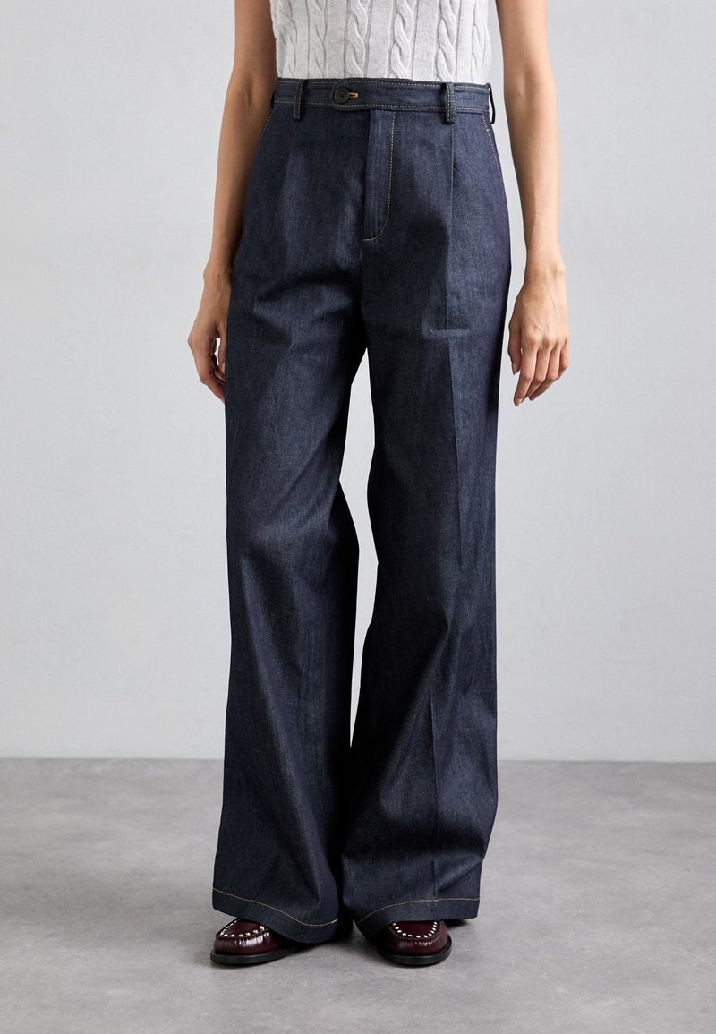 Pantalon en denim large coupe blue foncé avec une taille haute, arborant des coutures dorées et une fermeture à bouton à l'avant. Texture lisse et décontract�ée.