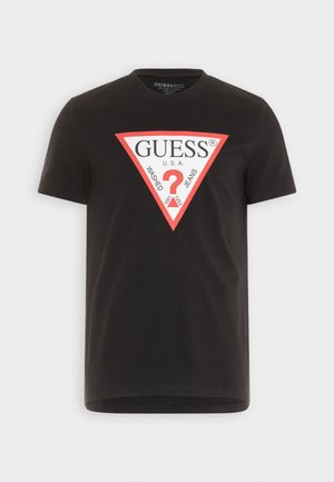 Sort bomulds-t-shirt med et rødt og hvidt trekantet grafisk design, der har teksten "GUESS" og "WASHED JEANS", korte ærmer og rund hals.