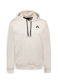 Sudadera color crema hecha de una tela suave, con un bolsillo frontal tipo canguro, capucha con cordón y un logo negro en el lado izquierdo del pecho.