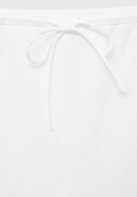 Biely sťahovací pás s mäkkou textúrou, s centrálnym uzlom. Tkanina pôsobí hladko a ľahko, s minimálnymi švami.