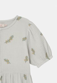Grå, strukturerad klänning i tyg med puffärmar, som har grön och gul blommig broderi och en rynkad kjol. Rund halsringning och knappdetalj.