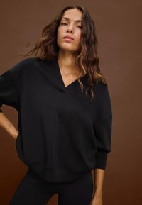 Felpa nera oversize con scollo a V, vestibilità morbida e maniche lunghe. Tessuto morbido, con maniche a sbuffo e orlo arrotondato.