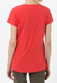 Camiseta corta roja de manga corta con cuello redondo, textura suave y un poco alargada en la parte de atrás, combinada con pantalones beige.