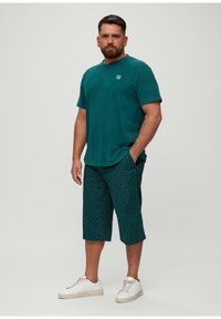 Teal katoenen T-shirt gekoppeld aan een patroon met donkerteal shorts met witte stippen. Draag het met witte sneakers voor een ontspannen look.