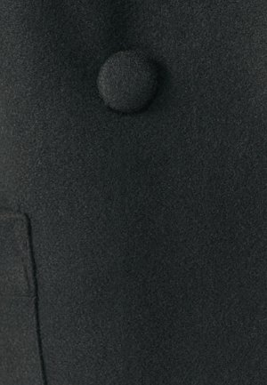 Abrigo de lana negro con un acabado texturizado, que presenta un botón redondo cubierto de tela y un bolsillo lateral para funcionalidad.