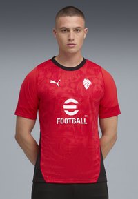 Rød fodboldtrøje med korte ærmer, der har et tekstureret mønster, sorte detaljer og en rund hals. Viser PUMA-logoet og et rundt logo med "FOOTBALL."