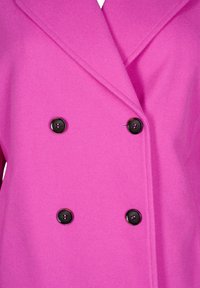 Rosa ullblandad kappa med dubbelknäppt design, snedställda slag och fyra svarta knappar som hårdvaruaccenter.