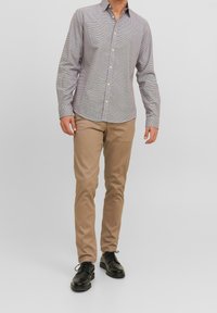 Bröstknappsskjorta i grå och vit rutig mönster, lång ärm, kombinerad med beige byxor och svarta skor. Tätt sittande design och slät textur.