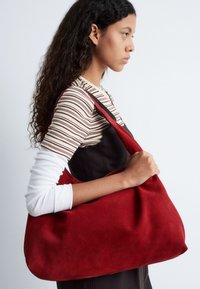 Red suede shoulder bag with a soft, curved shape and a single strap. The fabric has a smooth texture and minimal detailing.