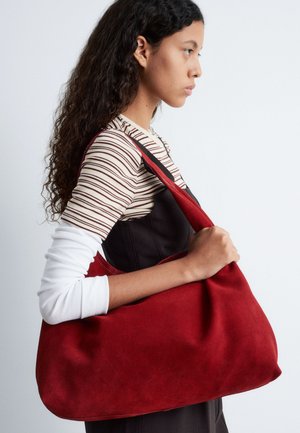 Rote Wildleder-Schultertasche mit einer weichen, geschwungenen Form und einem einzigen Riemen. Der Stoff hat eine glatte Textur und minimale Verzierungen.