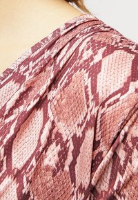 Fialová a růžová látka s vzorem hadí kůže a hladkou texturou. Obsahuje volný výstřih a detaily z vrstvené látky.