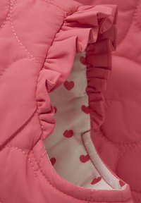 Rosa gesteppter Stoff mit einem Rüschkragen und einem weißen Futter, das mit roten Herzmustern bedruckt ist. Strukturelles Detail auf der äußeren Oberfläche.