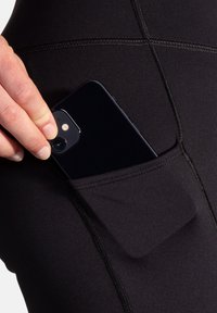 Leggings noirs avec une poche latérale contenant un smartphone, dotés de coutures à plat et d'une texture lisse. Poche conçue pour un accès facile.