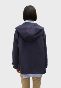 Navy blue hooded jacket with a loose fit, featuring a textured fabric and gold-tone accent buttons, worn over a light blue collared shirt.