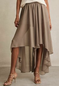 Gonna fluida alta-bassa in un tessuto taupe testurizzato. Presenta una vita elastica e rouches a strati all'orlo. Abbinata a sandali con tacco color sabbia.