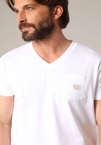 Witte katoenen V-hals t-shirt met korte mouwen, voorzien van een klein zakje en logodetail op het zakje. Soepele textuur.