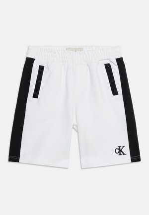 Valkoiset urheilushortsit mustilla sivupaneleilla, kaksi etutaskua vetoketjulla, joustava vyötärö ja pieni "cK"-logo vasemmassa lahkeessa.