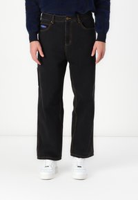 Sorte denim jeans med lige ben, prydet med kontrasterende gule sømme, en knaplukning og sidelommer. Båret med hvide sneakers.