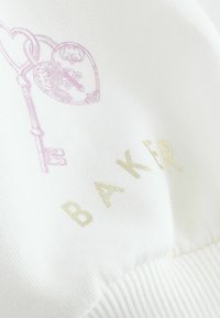 Valkoinen kangas, jossa vaaleanpunainen avain- ja sydänkuvio, ja sana "BAKER" kullassa. Sileä pinta ja resorireuna.