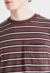 Striped short-sleeve T-shirt in maroon, white, and navy. Features a round neckline and a chest pocket. Soft cotton fabric.