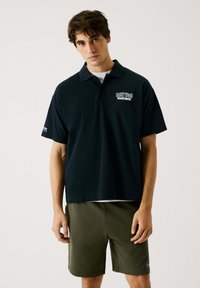 Zwarte polo met korte mouwen, voorzien van een logo op de linkerkant van de borst, gecombineerd met olijfgroene shorts. Gemaakt van katoen, in een relaxte fit.