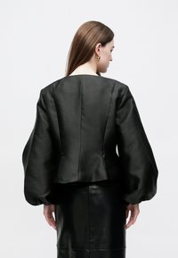 Jachetă neagră din satin cu o siluetă structurată, mâneci largi bufante și decolteu rotund. Prezintă o textură netedă și croială ajustată.