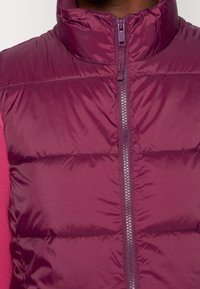 Bordeauxfärgad pufferväst med hög krage, horisontell quiltad design och dragkedja framtill. Tillverkad av glänsande nylonmaterial, utan anmärkningsvärda mönster.