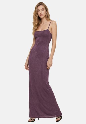 Abito viola aderente, lungo fino al pavimento, con spalline sottili, indossato da una donna in piedi con capelli lunghi e mossi e tacchi neri aperti in punta.