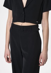 Zwarte geknipte blouse met knopen en korte mouwen, gecombineerd met high-waisted broek met een riem, een gladde textuur en een op maat gemaakte pasvorm.