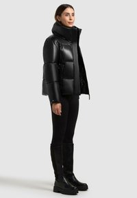 Sort puffers jakke med høj krave, quiltet design, blank finish og sidelommer, parret med sorte tætsiddende leggings og støvler til knæene.