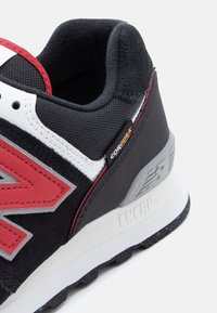 Κοντινό πλάνο της φτέρνας αθλητικού παπουτσιού σε μαύρο, λευκό και κόκκινο με επενδεδυμένο γιακά, ετικέτα υφάσματος «CORDURA» και υφασμένο λευκό πάτο με τη σήμανση «ENCAP».