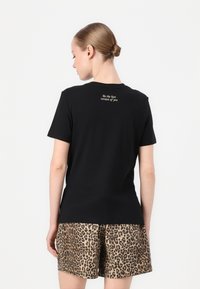 Melna kokvilnas t-kreklā ar īsām piedurknēm un apaļu kaklu, ar baltu izšūtu tekstu augšējā mugurā. Apvienots ar leopardu raksta šortiem.
