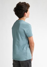 Camiseta de manga corta azul celeste hecha de algodón, con escote redondo y textura suave. La vista posterior muestra un ajuste relajado.