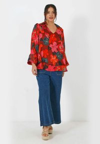 Rode bloemetjesblouse met bell sleeves en V-hals, gecombineerd met wijde blauwe denim jeans. De outfit heeft een lichte, vloeiende textuur.