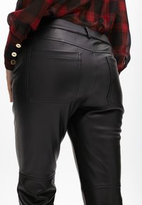 Pantaloni in pelle nera con una texture liscia, dotati di tasche posteriori e un design aderente. Vita alta con dettagli di cucitura sottili.