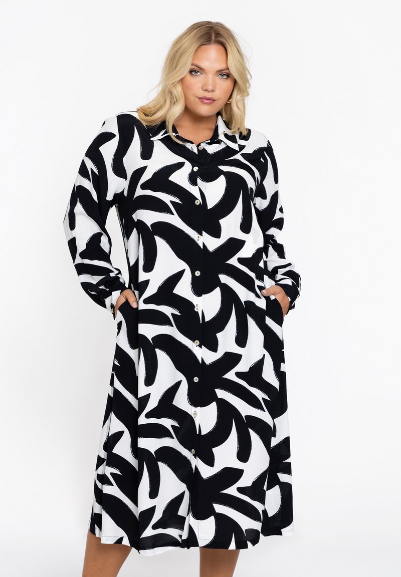 Schwarz-weißes Hemdkleid mit einem abstrakten Blattmuster, langen Ärmeln und seitlichen Taschen. Glattes Fabric mit lässiger Passform.