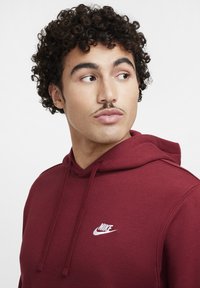 Bordeaux hoodie met een voorzak en trekkoordcapuchon, met een wit Nike-logo op de linkerborst. Zachte textuur, casual ontwerp.
