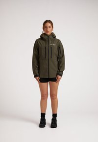 Giacca impermeabile verde oliva con cappuccio, tasche con zip e dettagli neri. Presenta polsini regolabili e un design aderente.