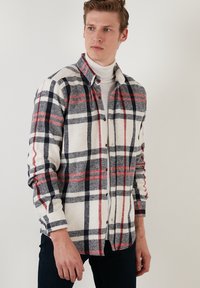 Geruite flanel shirt in crème, grijs en marineblauw, met rode en zwarte lijnen. Het heeft een knoopsluiting aan de voorkant en lange mouwen.