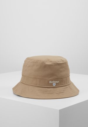 Chapeau bob en coton marron clair avec bord cousu et logo "Barbour" brodé sur le côté, posé sur une surface blanche.